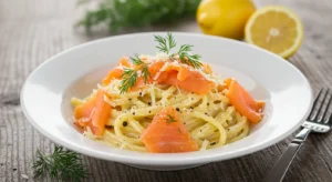 Smoked salmon pasta in a white bowl with creamy lemon sauce, topped with smoked salmon slices, fresh dill, and grated Parmesan on a rustic wooden table
