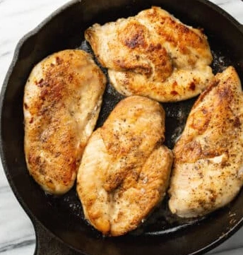 Golden-brown chicken breasts sizzling in a hot skillet with melted butter and garlic, creating a flavorful sear before adding the creamy garlic sauce
